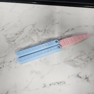 May include: A light blue and pink plastic butterfly knife. The knife is closed and has a textured design.