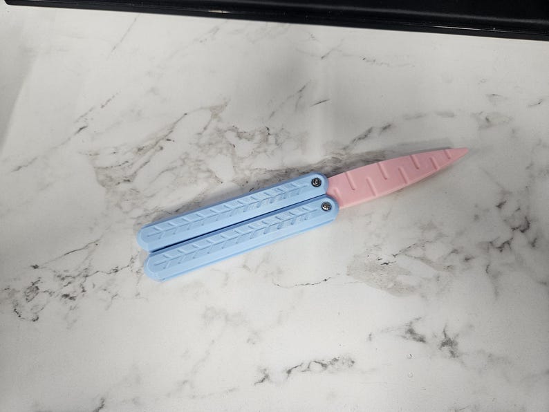 May include: A light blue and pink plastic butterfly knife. The knife is closed and has a textured design.