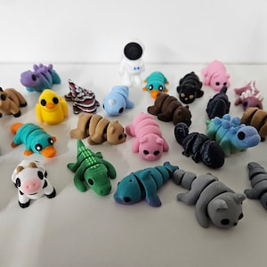 May include: A collection of 20 small, colorful, 3D printed animal figurines. The figurines are made of plastic and are about 2 inches tall. They include a variety of animals, such as a cow, a pig, a platypus, a turtle, a dinosaur, a fish, a bird, and a cat.