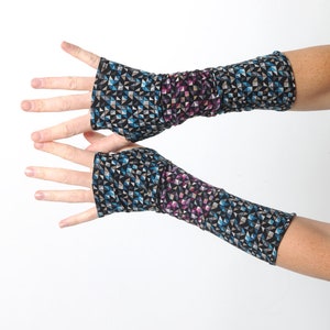 May include: A pair of fingerless arm warmers with a geometric pattern. The fabric features a repeating design of blue, black, gray, and purple triangles. The arm warmers are shown against a white background.