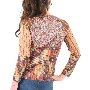 Peut inclure: Un chemisier à manches longues avec un motif patchwork composé de différents motifs dans des tons de brun, orange et rouge. Le chemisier a un col rond et une coupe ample.