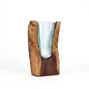 Könnte beinhalten: Ein durchsichtiges Glasgefäß mit unregelmäßiger, organischer Form ist in ein dickes, aufrecht stehendes Stück natürliches braunes Holz eingelassen. Das Holz hat eine raue, strukturierte Rindenaußenseite und eine glatte, polierte Innenseite.