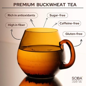 Könnte beinhalten: Eine gläserne Tasse gefüllt mit einer dunkelbernsteinfarbenen Flüssigkeit, beschriftet mit "PREMIUM BUCKWHEAT TEA". Der Tee wird als reich an Antioxidantien, ballaststoffreich, zuckerfrei, koffeinfrei und glutenfrei beschrieben.