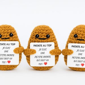 May include: Three crocheted potato figures, each holding a sign with French text. The potatoes are tan with black eyes and smiles. The signs read "PATATE AU TOP" and "JE SUIS UNE PETITE PATATE QUI CROIT EN TOI!" with a red heart.