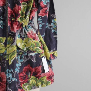 May include: A dark blue floral print jacket with a zipper closure and a drawstring waist. The jacket has a tag attached to the sleeve.