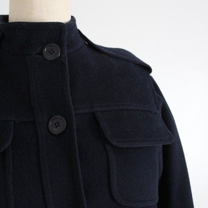May include: A navy blue wool jacket with a stand-up collar, flap pockets, and button closures.