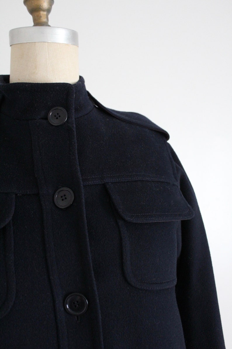 May include: A navy blue wool jacket with a stand-up collar, flap pockets, and button closures.