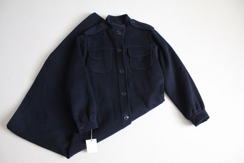 May include: A navy blue long-sleeved jacket with a stand-up collar, four pockets, and button closures.