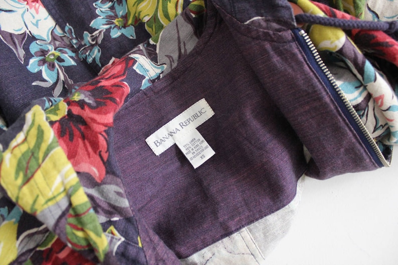 May include: A purple hooded jacket with a floral print and a zipper closure. The jacket has a label that reads "Banana Republic" and a size tag that reads "XS".