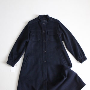 May include: A long navy blue coat with a stand-up collar, button closure, and two large flap pockets.