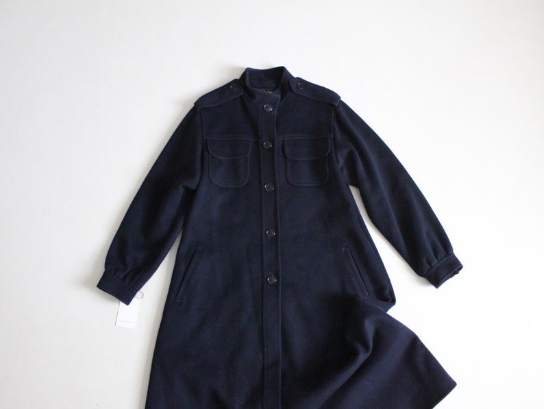 May include: A long navy blue coat with a stand-up collar, button closure, and two large flap pockets.