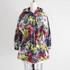 May include: A hooded jacket with a floral print in shades of pink, green, yellow, and blue. The jacket has a drawstring waist and a zipper closure.