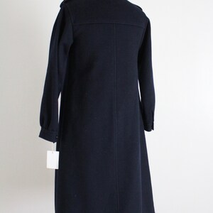 May include: A long, dark blue coat with a high collar and a single button closure. The coat has a slightly flared hem and is made of a thick, textured fabric.