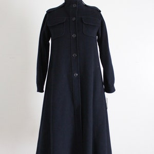May include: A long, navy blue coat with a button-up front and large pockets. The coat has a stand-up collar and a slightly flared skirt.
