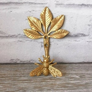 May include: Gold metal wall hook shaped like a tree with five leaves and a bee at the bottom.