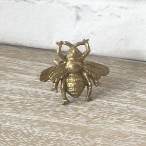 May include: A gold-toned metal bee-shaped drawer pull. The bee has detailed wings and legs.