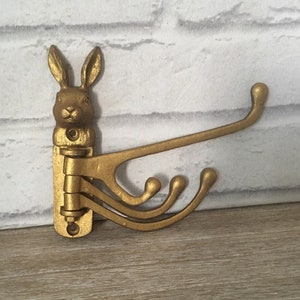 Puede incluir: Gancho de pared de metal dorado en forma de cabeza de conejo con cuatro ganchos que se extienden hacia un lado.
