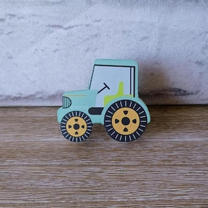 Könnte beinhalten: Ein hellblauer Holztrecker mit schwarzen und gelben Rädern. Der Traktor hat ein weißes Fenster und einen gelben Sitz. Der Traktor steht auf einer Holzoberfläche.