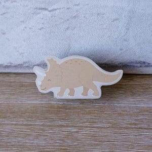May include: A brown cartoon triceratops dinosaur cutout. The dinosaur is facing left and has a white outline.