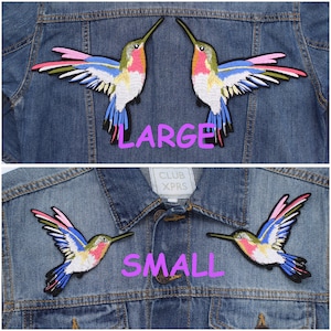 Puede incluir: Dos chaquetas vaqueras con parches bordados de colibríes. La chaqueta superior tiene dos parches grandes de colibríes y la palabra "LARGE" en rosa. La chaqueta inferior tiene dos parches de colibríes más pequeños y la palabra "SMALL" en rosa.