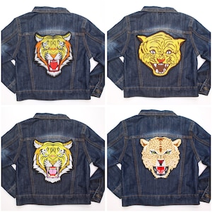 May include: Four denim jackets, each with a different embroidered tiger patch. The patches feature tiger designs in shades of orange, yellow, and tan. The jackets are a classic blue denim wash, with button closures and pockets.