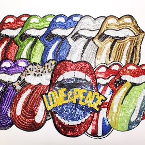 May include: A selection of sequined lips in diverse colours, such as red, green, blue, and gold. One set of lips displays the words "LOVE & PEACE" in yellow. The lips are a pop art design.