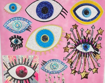 May include: A collection of sequined eye patches in various sizes and designs, featuring blue, white, yellow, and pink colors. Some patches have star and fringe accents, while others have a simple eye shape.