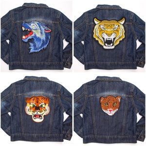 May include: Four denim jackets, each with an embroidered animal patch. The patches feature a blue wolf, a yellow and black tiger, an orange and black tiger, and a brown and orange tiger. The jackets are a medium wash denim.