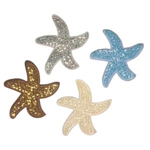 May include: Four sequined starfish in silver, blue, gold, and cream. Each starfish has five points and is filled with small, shiny sequins. The starfish are arranged against a white background, creating a nautical theme.