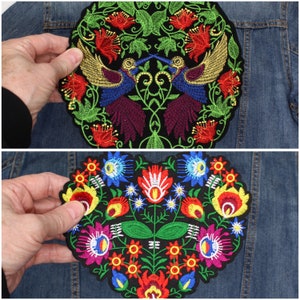 May include: Two embroidered patches with floral and bird designs. One is round with two birds facing each other, surrounded by red flowers and green leaves. The other is heart-shaped, featuring colourful flowers and leaves.