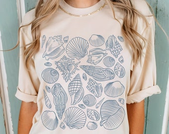 Op de afbeelding: Beige T-shirt met een blauw schelpenontwerp. Het ontwerp toont verschillende schelpenillustraties in verschillende vormen en maten. Het T-shirt heeft korte mouwen en een relaxte pasvorm, ideaal voor dagelijks gebruik.