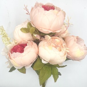 May include: A bouquet of six blush pink peonies with red centers. The peonies are arranged in a cluster with green leaves.