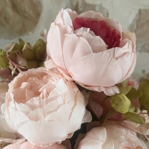 May include: A bouquet of pink and white peonies with green leaves. The peonies are in full bloom and have a delicate, ruffled texture.