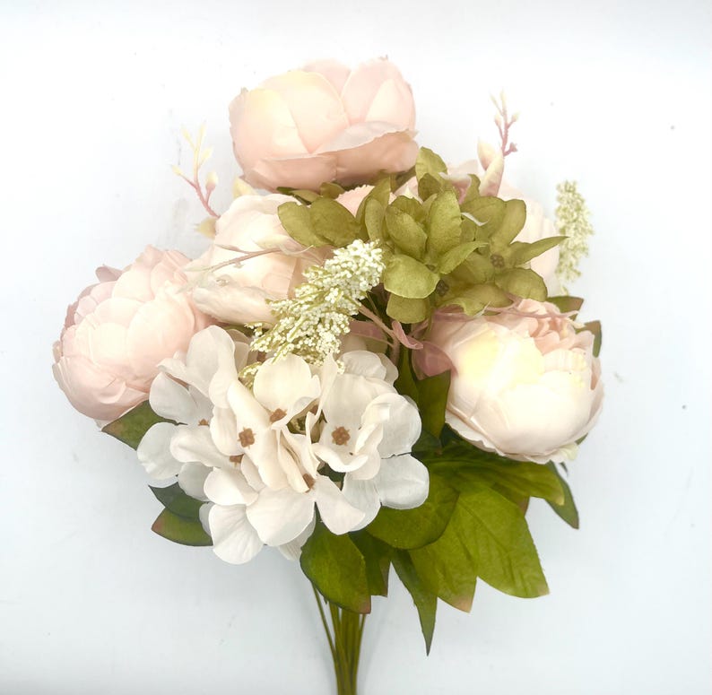 May include: A bouquet of artificial flowers with pink peonies and white hydrangeas. The bouquet is accented with green leaves and small white flowers.