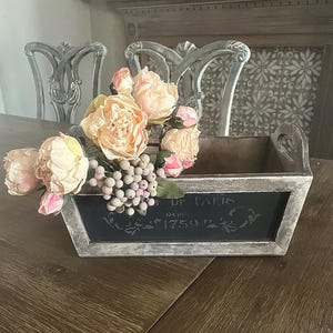 May include: A rectangular wooden planter with a distressed gray and white finish, holding a bouquet of peach and pink flowers. The front of the planter has a black chalkboard-style panel with the text "DE PARIS 1759".