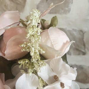 May include: A close-up of a pink and white artificial flower arrangement. The arrangement features delicate pink roses and white hydrangeas with green foliage.
