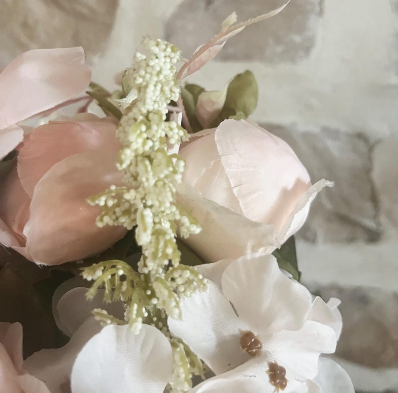 May include: A close-up of a pink and white artificial flower arrangement. The arrangement features delicate pink roses and white hydrangeas with green foliage.