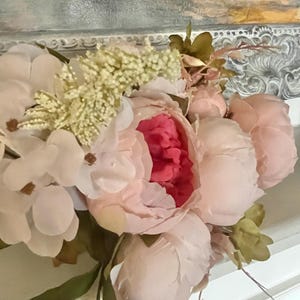May include: A bouquet of pink and white silk flowers with green leaves. The flowers are arranged in a vase and are sitting on a white surface.