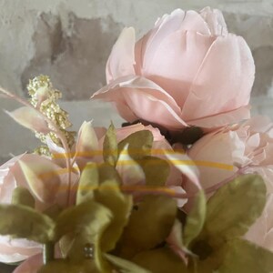 May include: A bouquet of pink silk peonies with green leaves. The peonies are arranged in a cluster, with the leaves surrounding them.
