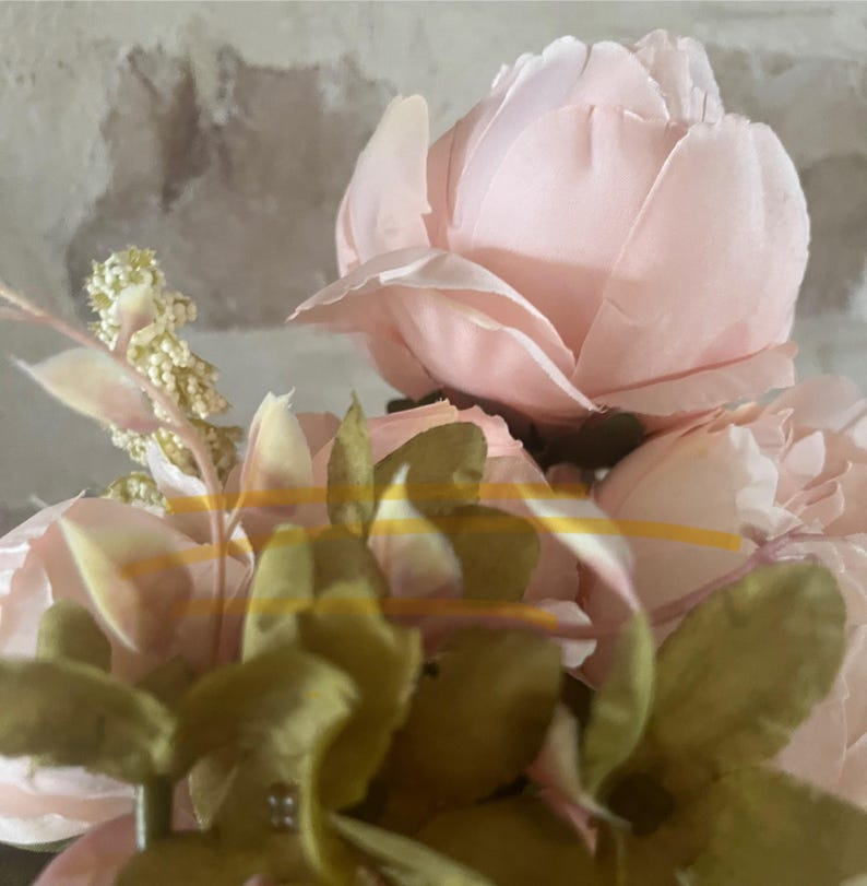May include: A bouquet of pink silk peonies with green leaves. The peonies are arranged in a cluster, with the leaves surrounding them.