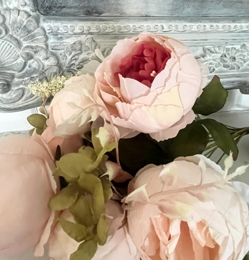 May include: A bouquet of pink peonies with green leaves. The flowers are arranged in a vase and are in focus. The background is out of focus.
