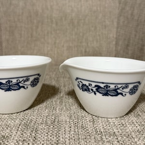 Peut inclure: Deux bols de service en céramique blanche avec un motif floral bleu. L'un est de forme standard, l'autre a un bec et une poignée. Les bols sont probablement destinés à servir des sauces ou des condiments.