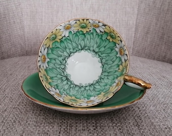 May include: A vintage teacup and saucer set with a green and white floral design. The cup features a white centre with a green and white floral border. The saucer is a solid green colour.