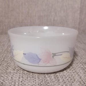 Puede incluir: Tazón de cerámica blanco con un diseño floral con hojas rosas, moradas y amarillas. El tazón tiene un acabado liso y brillante.