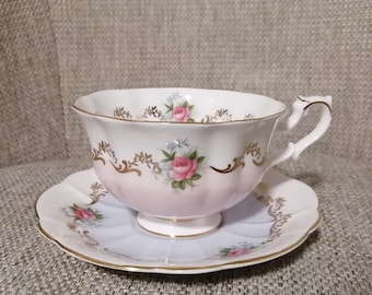 Pode incluir: Um conjunto de chávena e pires rosa com um design floral. A chávena tem uma borda ondulada e uma pega delicada. O pires tem um design floral correspondente e uma borda ondulada.
