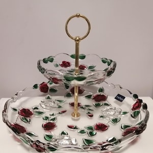 Puede incluir: Bandeja de servir de vidrio de dos niveles con un soporte de metal dorado. La bandeja presenta un diseño floral con rosas rojas y hojas verdes.