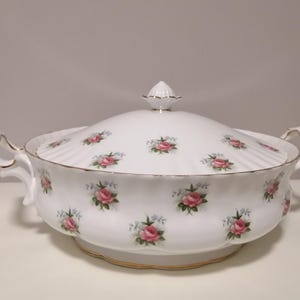 May include: White porcelain serving dish with a lid, featuring a floral pattern of pink roses and green leaves. The dish has a scalloped edge and gold trim.