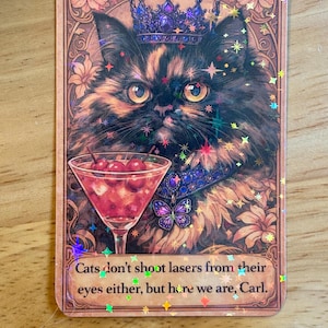 Könnte beinhalten: Ein rechteckiger Aufkleber mit einer königlichen Katze, die eine Juwelenkrone und einen Kragen trägt und einen Cocktail mit Kirschen hält. Der Aufkleber hat eine Vintage-Ästhetik mit floralen und sternförmigen Akzenten und dem Text "Cats don't shoot lasers from their eyes either, but here we are, Carl."