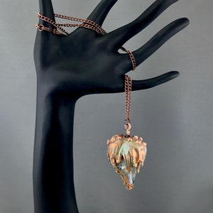 May include: A copper chain necklace with a unique pendant. The pendant is a teardrop shape with a clear crystal inside and a copper-colored exterior. The pendant has a textured, dripping effect.