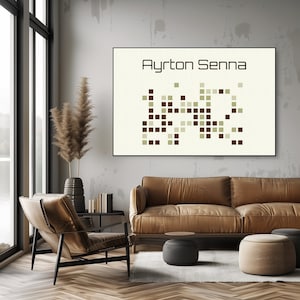 Könnte beinhalten: Ein braunes Ledersofa mit einem grauen Kissen in einem Wohnzimmer mit einem großen Fenster mit Blick auf einen See und einem gerahmten Druck an der Wand, auf dem "Ayrton Senna" steht, mit einem pixeligen Bild der Zahl "1" in braunen und grünen Quadraten.